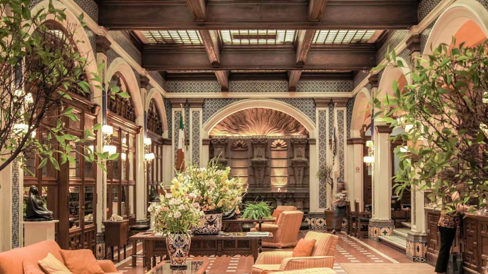 A luxurious hotel lobby featuring elegant architecture, rich decor, and comfortable seating under a stained glass ceiling.