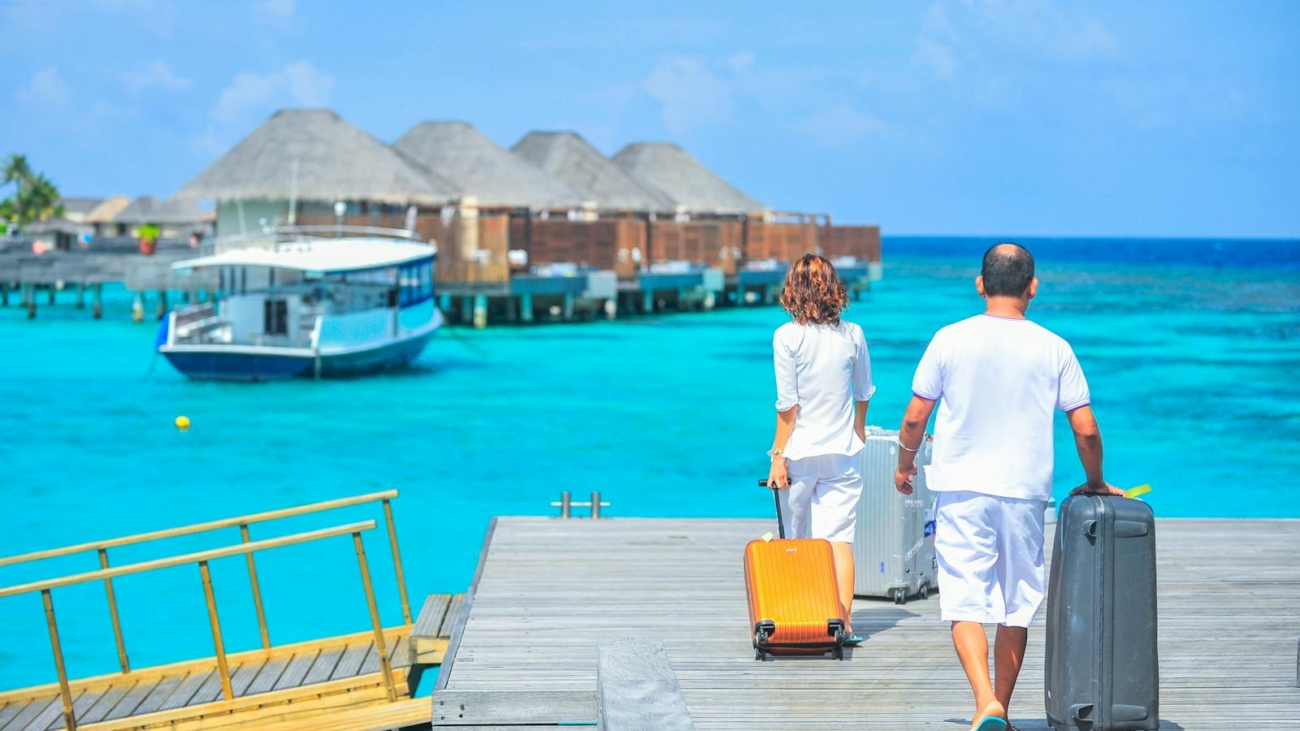 A couple arriving at a luxurious Maldives resort dock with luggage, capturing a tropical vacation vibe.