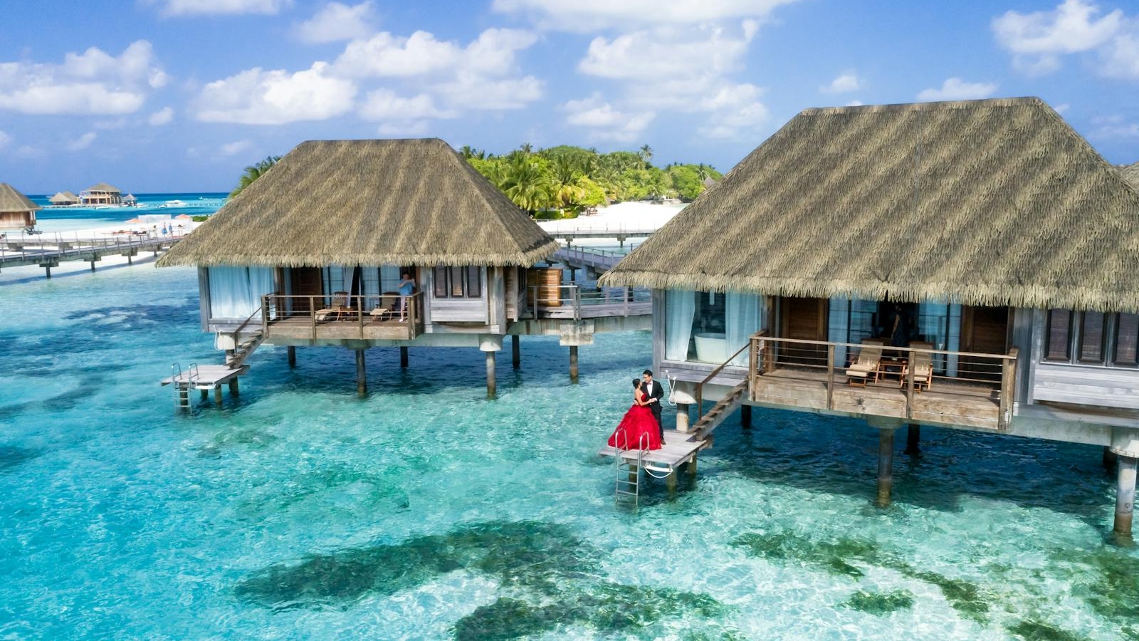 A scenic view of overwater bungalows and a couple enjoying a tropical paradise in the Maldives.