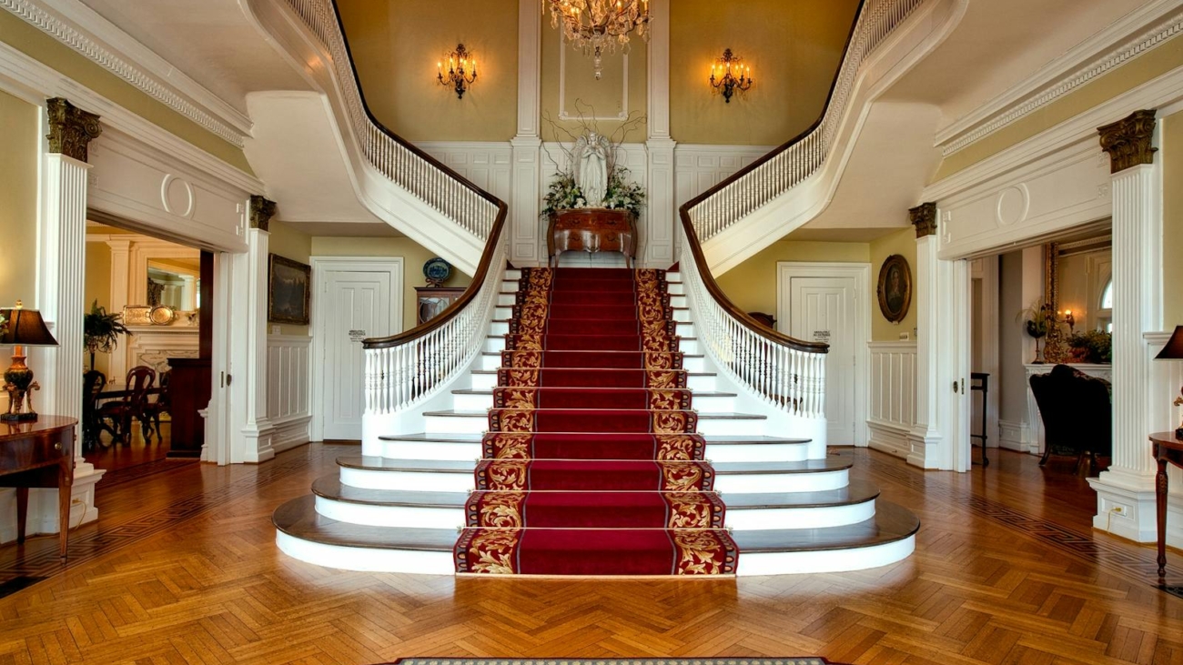 Grand staircase with red carpet in a luxurious hotel lobby, highlighted by a chandelier.