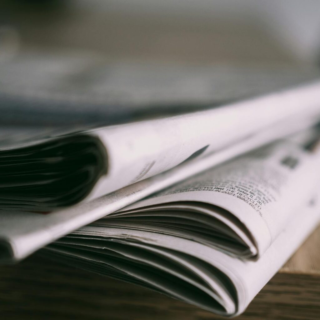 Stack of folded newspapers on a wooden table with a focus on printed pages.