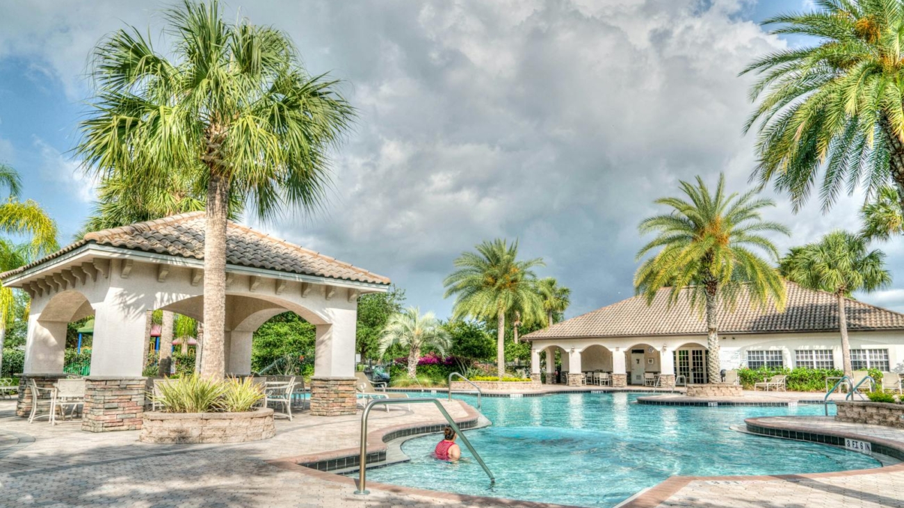 Beautiful tropical resort poolside scene featuring palm trees and inviting water under a cloudy sky.