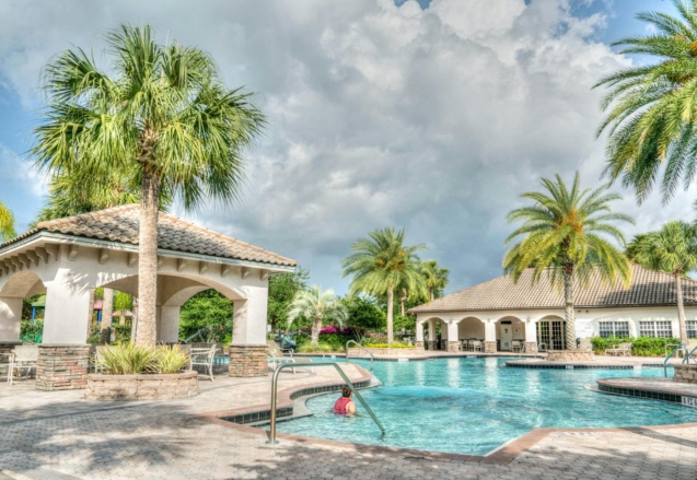 Beautiful tropical resort poolside scene featuring palm trees and inviting water under a cloudy sky.