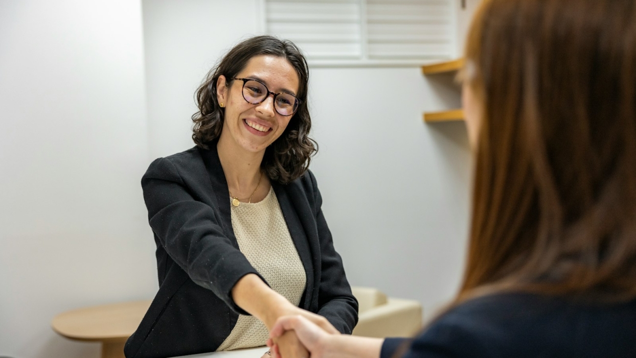 a woman shaking hands with another woman sitting at a table