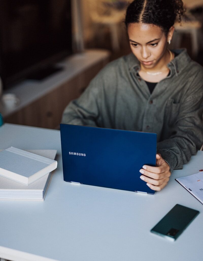 woman in gray jacket holding blue laptop