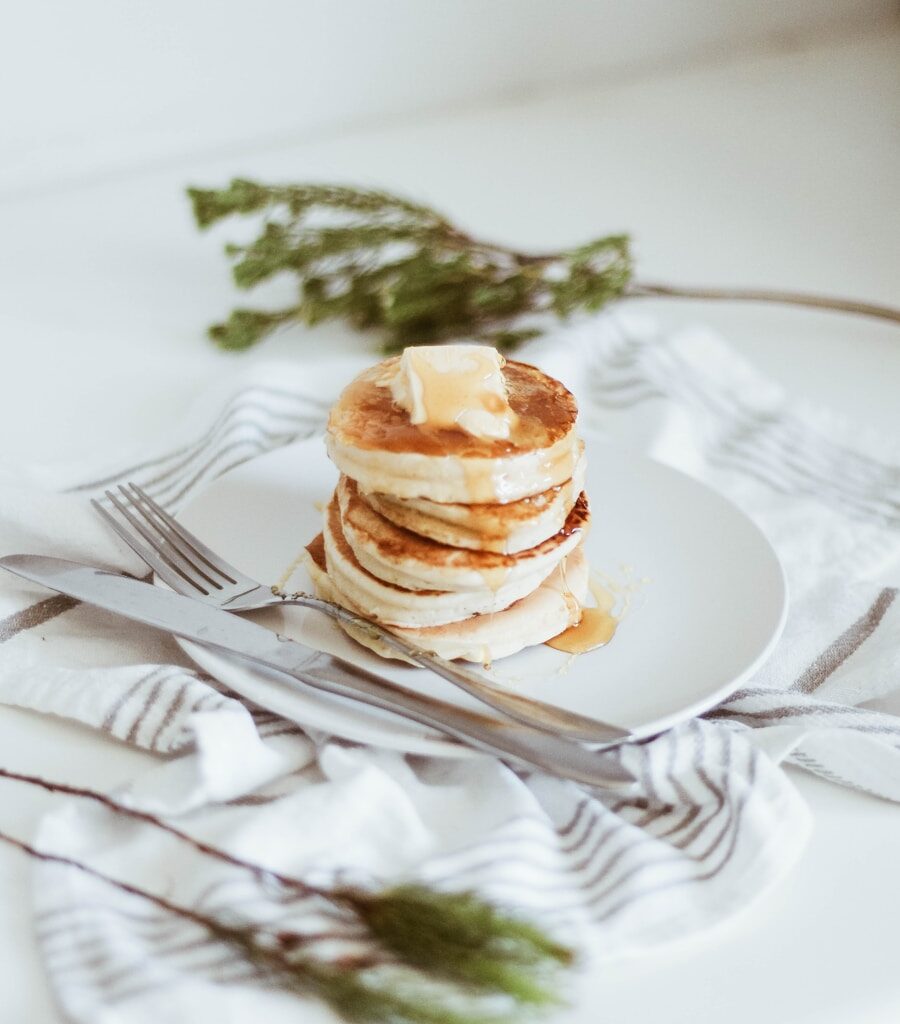 cooked pancake on round white ceramic plate beside butter knife and fork