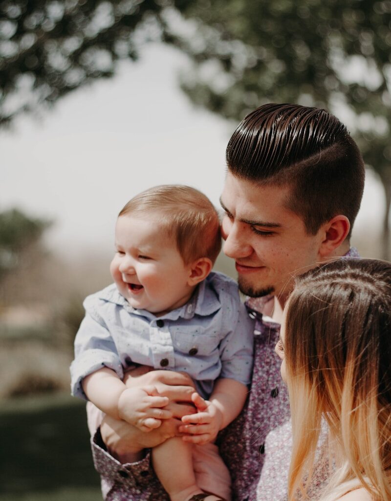 man carrying baby beside woman while smiling to each other