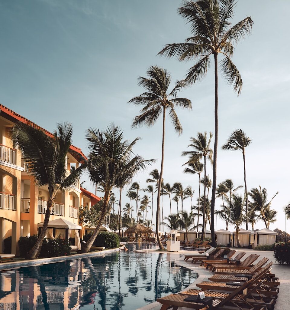 brown wooden lounge chairs near pool surrounded by palm trees