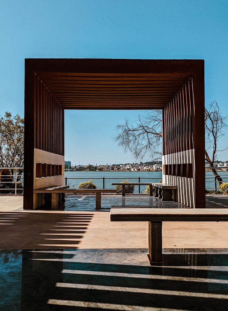 a bench sitting under a wooden structure next to a body of water