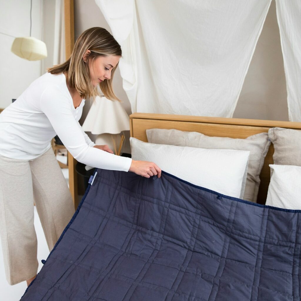 a woman putting a blue blanket on top of a bed